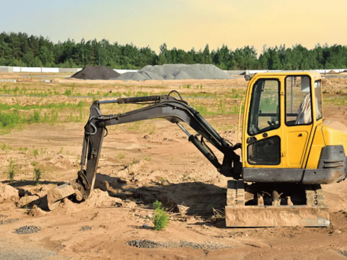 Mini excavator at construction site. Backhoe on earthwork. Digg trench to lay cables concrete curbs and paving slabs. Loader on roadworks on sunset background